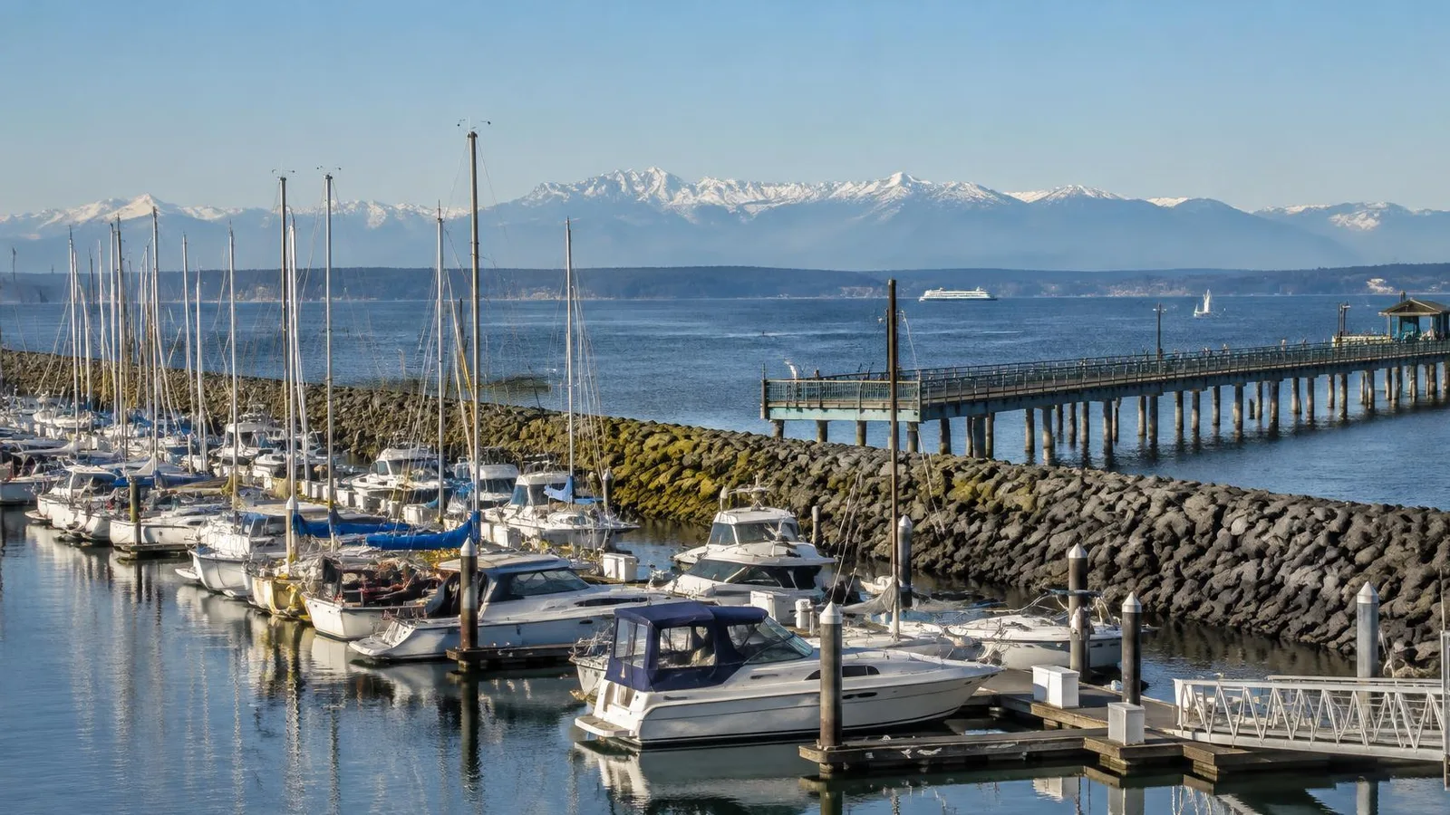 A vibrant marina with sailboats at sunset, with the Puget Sound and mountains in the distance